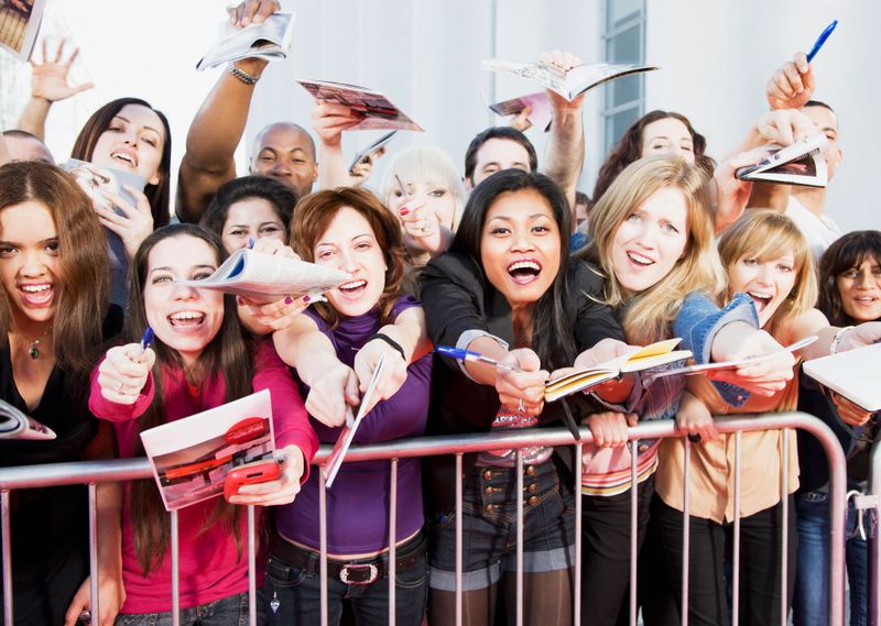 Fans offering notepads for celebrity's signature behind barrier