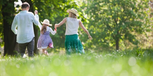 Family holding hands and walking in a sunny park.