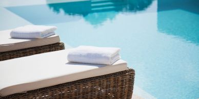 Two wicker poolside lounge chairs with white towels by a clear blue pool.