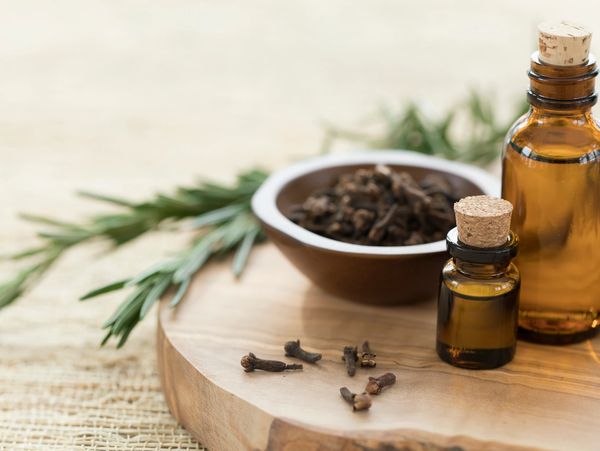 Essential oil bottles and cloves on a wooden board with herbs.