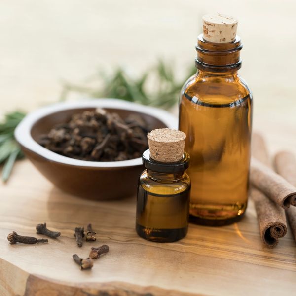 Amber bottles with corks, cloves, cinnamon sticks, and herbs on a wooden surface.