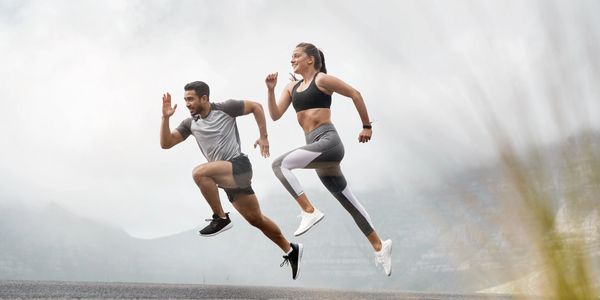 A man and woman sprinting outdoors, mid-air with determination.