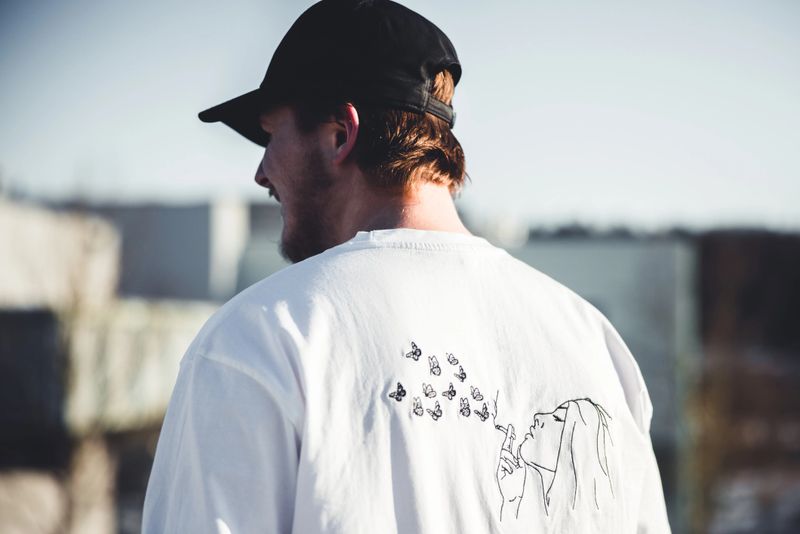 Young fashionable man with property released handmade craft designer t-shirt standing outdoors looking towards the city street. Shot from behind. Millennial Generation Male Young Fashion Design Portrait,