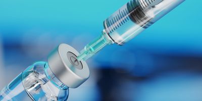 Syringe drawing liquid from a vial against a blue background.