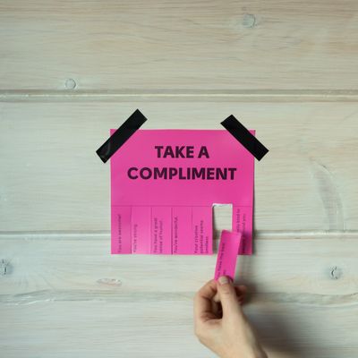 A hand takes a compliment tab from a pink paper posted on a wall.