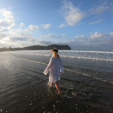 Woman in a hat walking in shallow ocean water at sunrise.