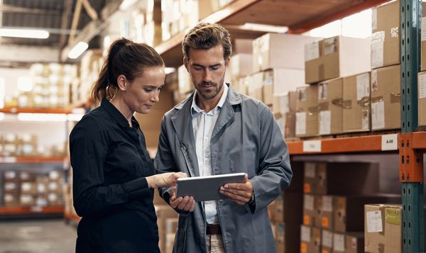 Two warehouse workers checking inventory on a tablet.