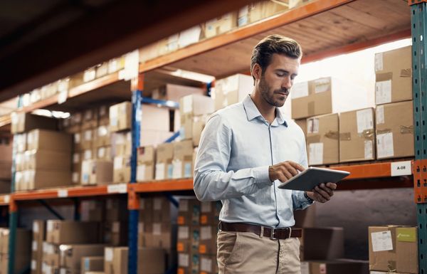 A man in a warehouse using a tablet for inventory management.