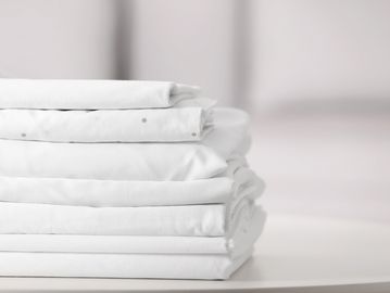 A neatly folded stack of white bed linens on a white surface.