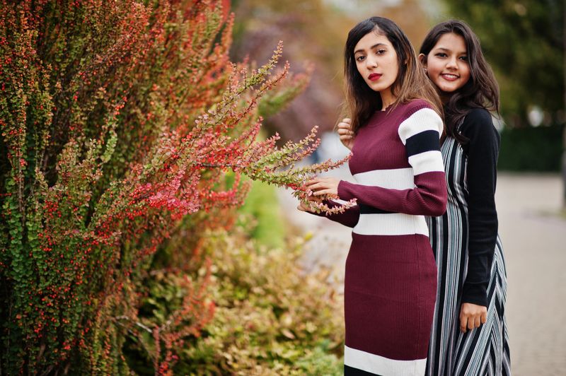 Portrait of two young beautiful indian or south asian teenage girls in dress posed near bushes.