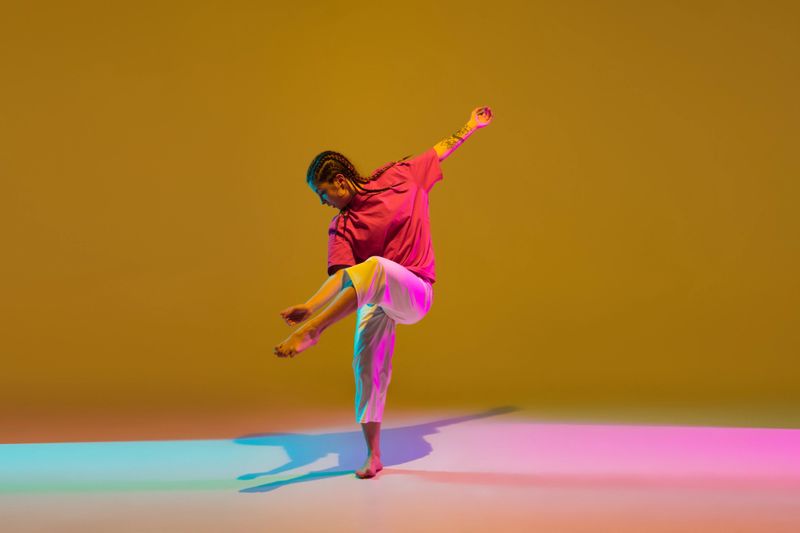 Street style. Hip-hop dancer young Caucasian girl dancing in stylish red and white attire over colorful background in neon light. Youth culture, fashion, action, healthy lifestyle. Copy space for ad.