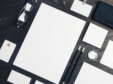 Blank stationery set with glasses and pencils on dark surface.