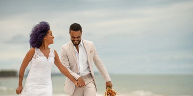 Happy couple in wedding attire walking hand in hand on the beach.