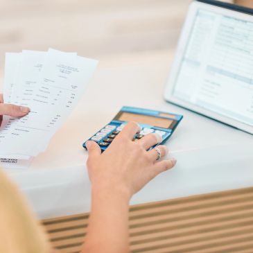 Person calculating bills with calculator and laptop.