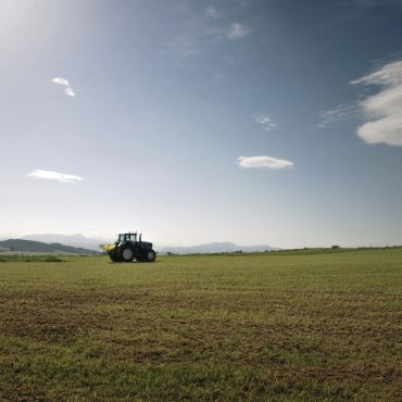 Tractor in a vast green field under a clear blue sky.