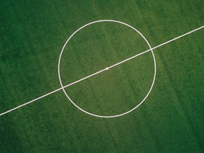 Aerial view of a soccer field's center circle and halfway line on green grass.