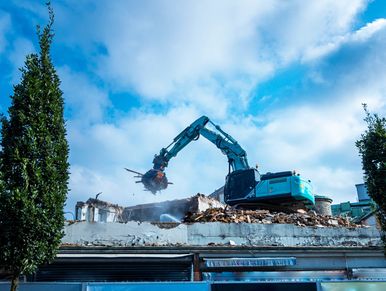 Excavator demolishing a building under a bright blue sky.