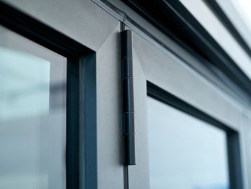 Close-up of a black metal door hinge on a modern glass door.