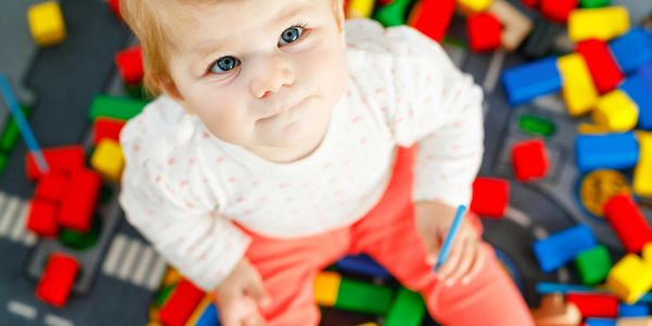 A baby with blue eyes sits among colorful building blocks.