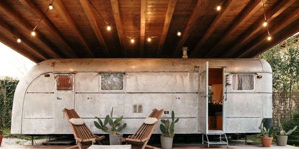 Vintage trailer under a wooden roof with cozy seating and string lights.