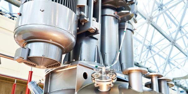 Close-up of industrial machinery with metal pipes and a motor inside a bright facility.
