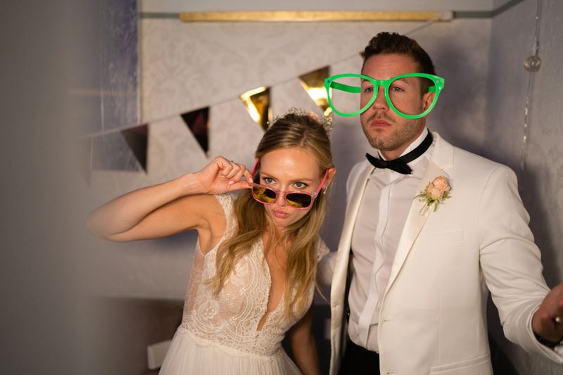 newly married wedding couple, bride in beautiful wedding dress, bridegroom in white dinner jacket, enjoying party and taking pictures at photo booth in the evening