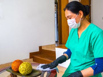 Woman cleaning glass table wearing gloves and mask.