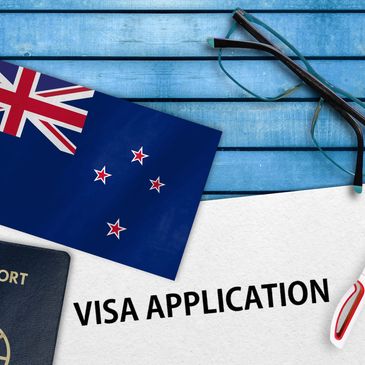 New Zealand visa application with passport, flag, glasses, and pen on blue wooden table.