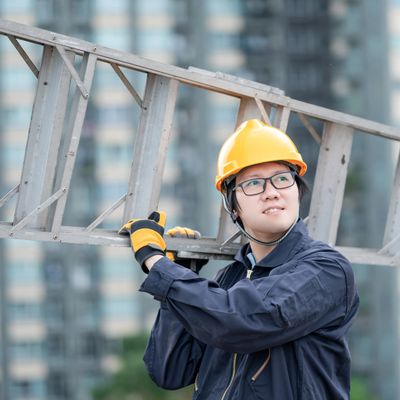 Construction worker carrying a ladder outdoors in safety gear.