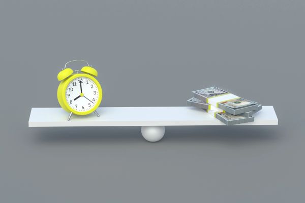 A yellow alarm clock balancing stacks of money on a seesaw.
