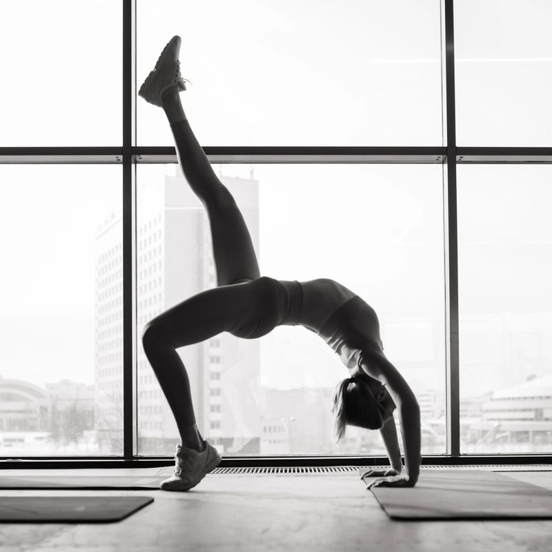 Woman practicing advanced yoga on mat against a large window