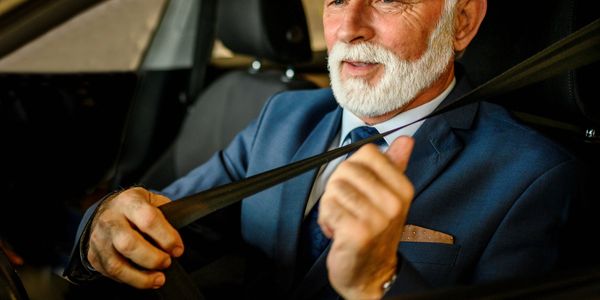 Senior man in a suit fastening his seatbelt inside a car.