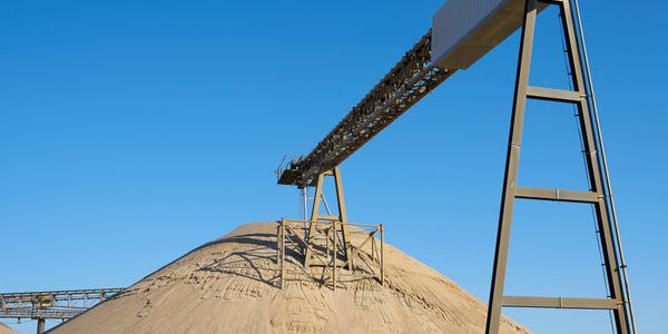 Large sand pile with conveyor system under clear blue sky.