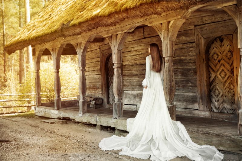 Wedding Bride Dress Rear View Outdoors. Vintage White Bridal Gown Back side View over Wooden Terrace with Column. Romantic Woman Portrait Outside