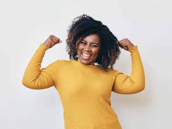 Woman in yellow sweater flexing muscles joyfully.