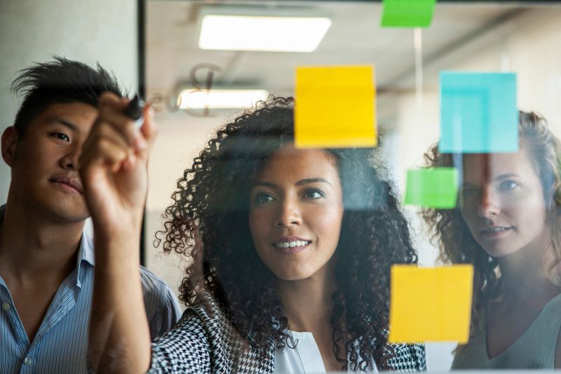 Smiling businesswoman writing on glass wall with felt tip pen while standing in office