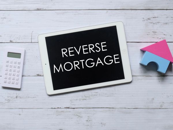 Tablet displaying 'REVERSE MORTGAGE' with calculator and house model.