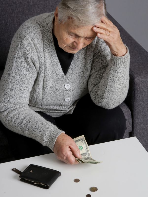 Elderly woman looks worried while counting money on a table.