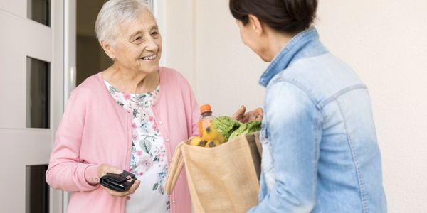 An elderly woman smiling while a younger woman holds grocery bag
