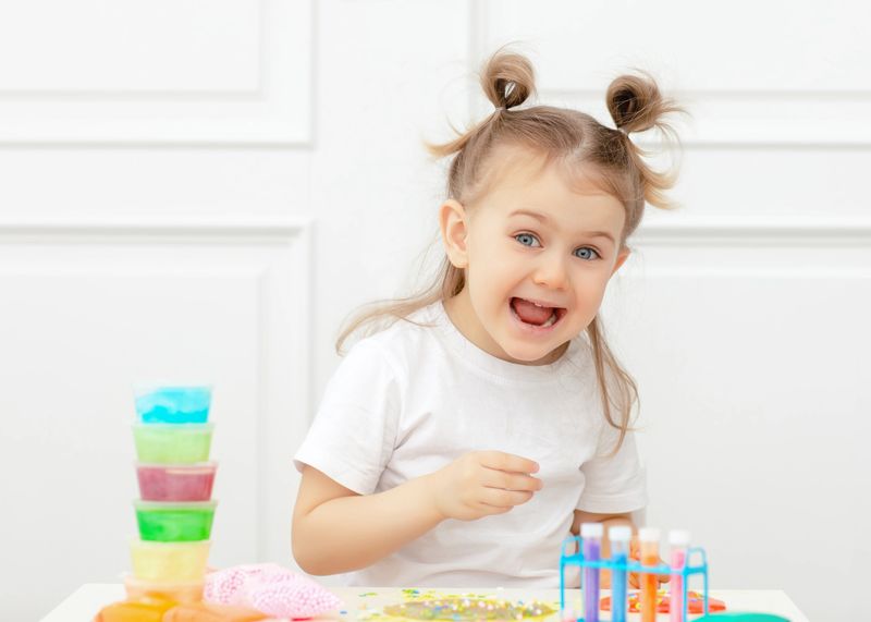 Emotional, smiley, adorible little child looks surprised, happy and joy into the camera to kindergarten. Concept of developing kid skills and learn. Scientist having fun making slime in the laboratory.