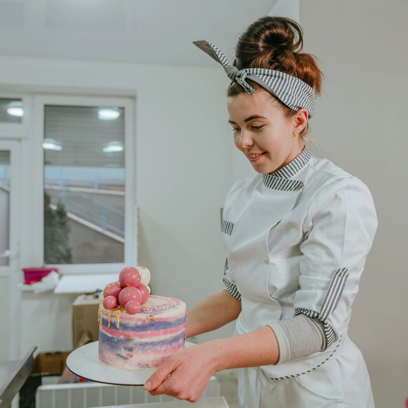 Female confectioner holding colorful birthday cake with chocolate balls in the confectionery studio