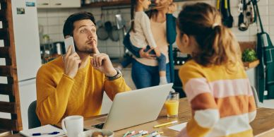 Man talking on phone while a woman and child wait in kitchen.