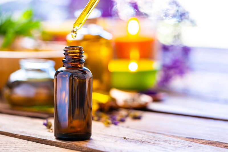 Health care and medicine: close up view of an essential oil bottle with a drop falling from a dropper shot on rustic wooden table. Selective focus on the bottle. The composition is at the left of an horizontal frame leaving useful copy space for text and/or logo at the right. Concepts  for aromatherapy, body care and well being. High resolution 42Mp studio digital capture taken with Sony A7rII and Sony FE 90mm f2.8 macro G OSS lens