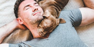 Man lying down with a puppy cuddling his neck peacefully.