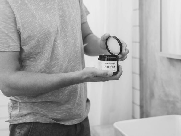 Man holding an open jar of face cream in a bathroom.