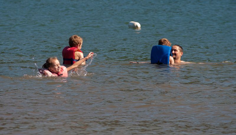 Summer family fun kids wearing lifejackets play in the lake water with father