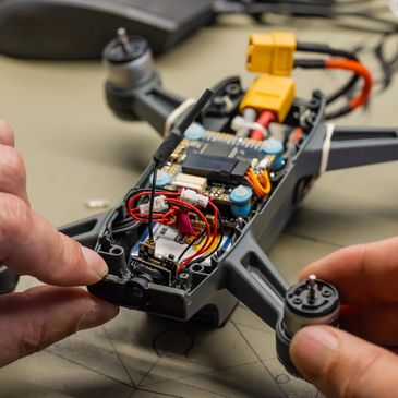 Hands assembling a small drone with visible circuit board and wiring.