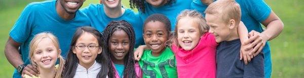 Diverse group of happy children and adults smiling outdoors in casual clothes.