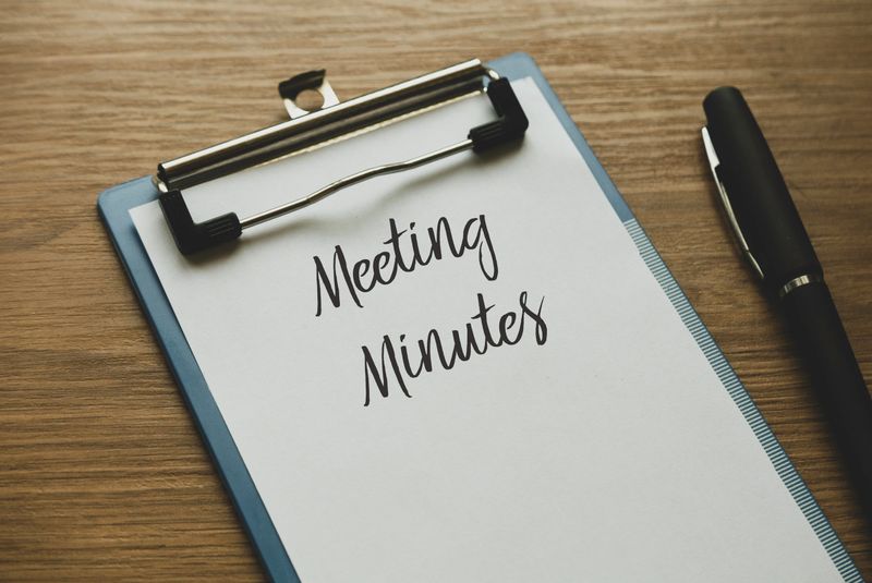 Selective focus of a pen and clipboard with paper written with Meeting Minutes on wooden background.