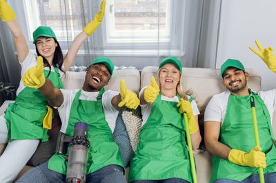 A happy group of cleaners in green aprons posing with cleaning tools on a couch.